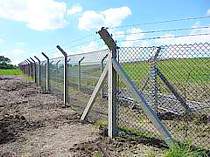 Chain link fence on concrete fence posts with cranked arm tops supporting 3no. strands of barbed wire