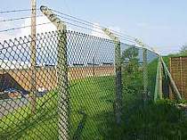 Chain link fence on concrete fence posts with cranked arm tops supporting 3no. strands of barbed wire