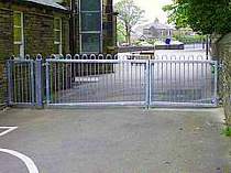Double leaf galvanised bow top vertical bar entrance gates - bottom of gates fabricated to suit the sloping ground under the gates