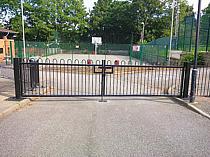 Double leaf black powder coated bow top access road gates - bottom of gates fabricated to suit the sloping ground under the gates