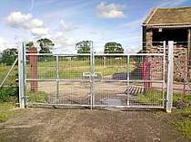 Double leaf galvanised entrance gates in-filled with welded mesh and vertically extended with 3no. strands of barbed wire