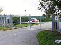 Galvanised welded mesh in-filled double leaf entrance gates - tops of gates vertically extended with 3no. strands of barbed wire