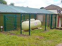 Green powder coated V-beam mesh panel fence compound around a propane gas supply cylinder - fence incorporates 2 access gates