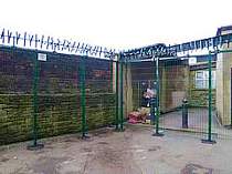 Green powder coated V-Beam mesh panel fencing fitted at a special needs school - fence incorporates additional fence posts# mesh clamp bars instead of the usual fence clips and a top row of rotating spikes